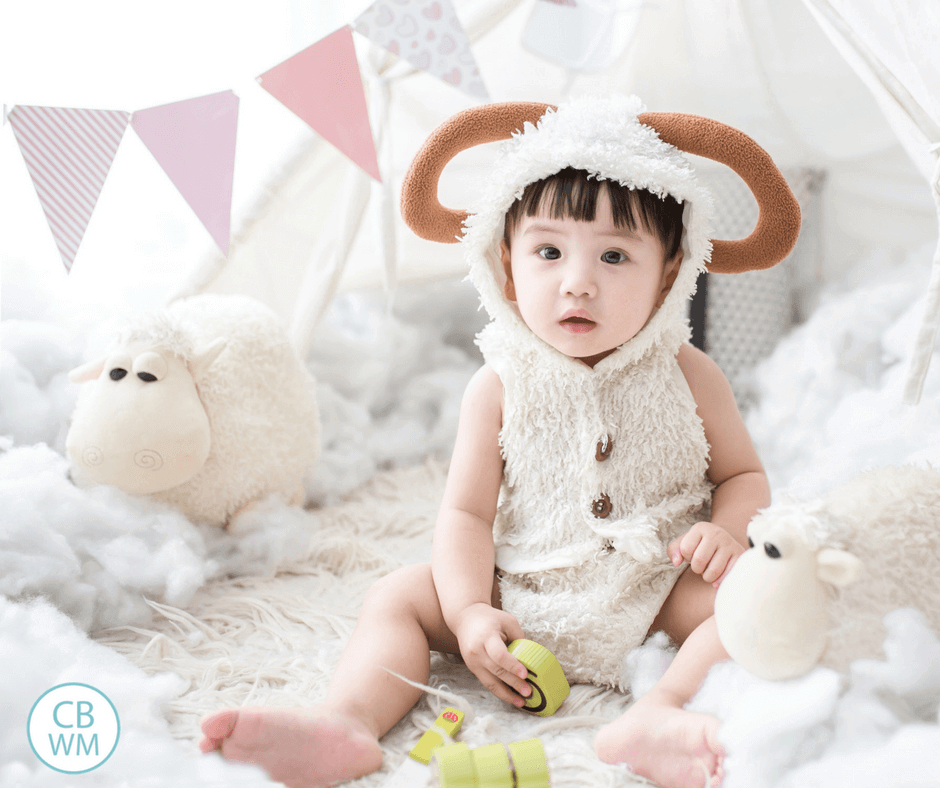 baby in lamb costume sitting with lamb stuffed animals