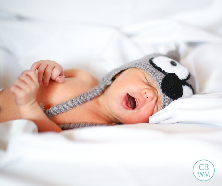 Baby sleeping in a hat on white bedding with mouth open