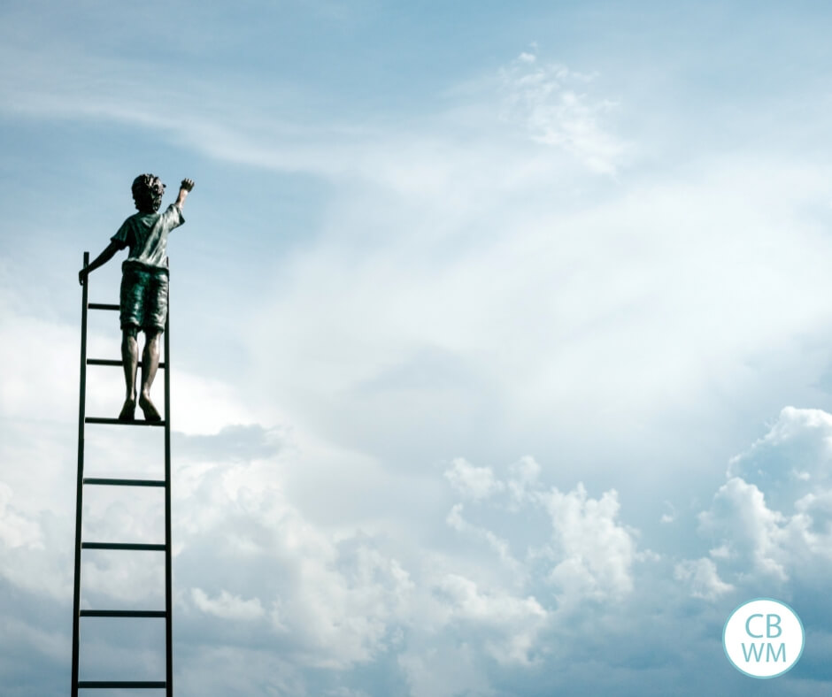 Child reaching for the clouds while standing on a ladder