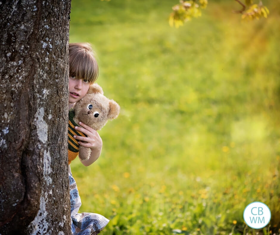 A girl hiding behind a tree holding a bear