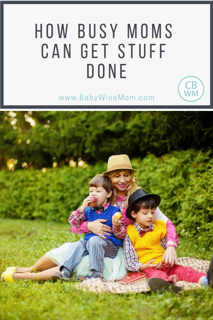 Mom with two boys sitting on a blanket on the grass with text Tips for moms to be productive and get things done. Cleaning schedule tips, daily life tips, and a sample daily schedule of a SAHM. 