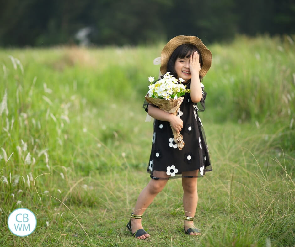 Girl standing in a green meadow holding a bouquet of flowers