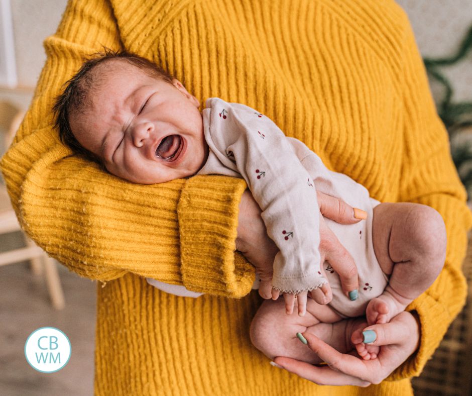 Woman wearing a mustard yellow sweater holding a crying newborn in her arms