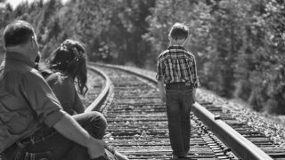 Child walking down the railroad tracks as parent watch