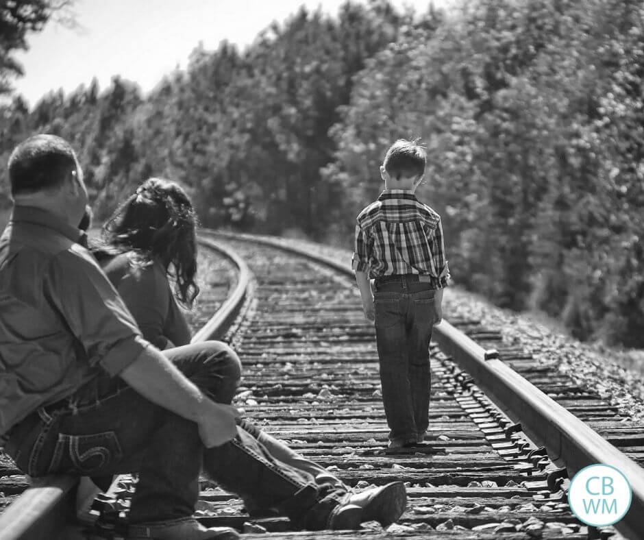 Child walking down the railroad tracks as parent watch