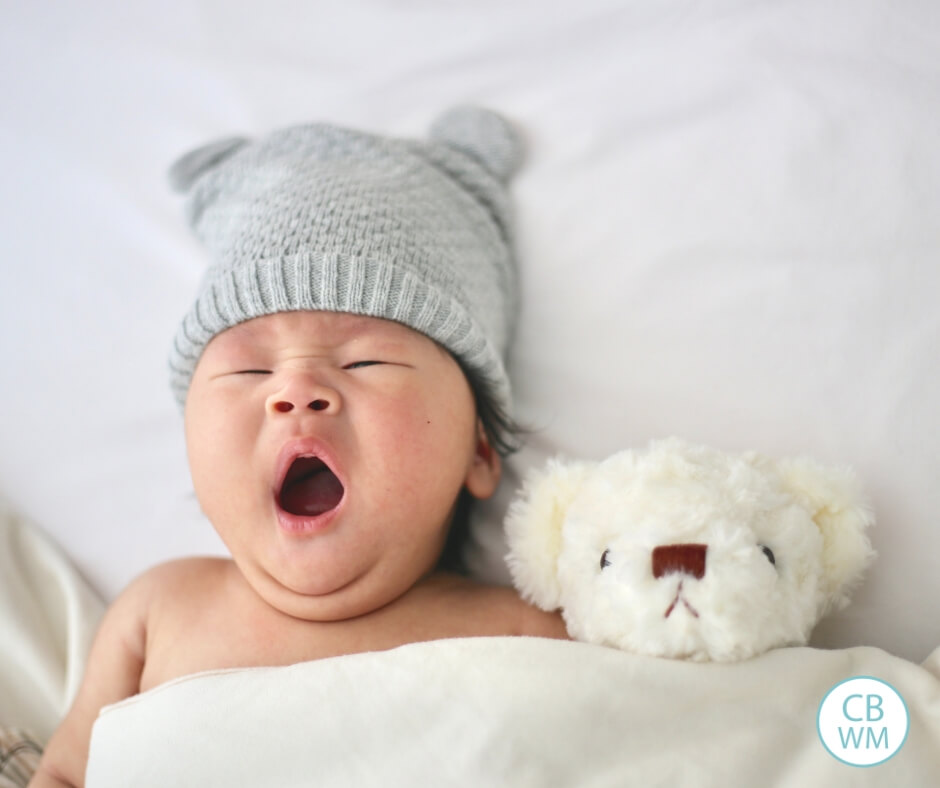 Bebé bostezando en la cama junto a un oso de peluche