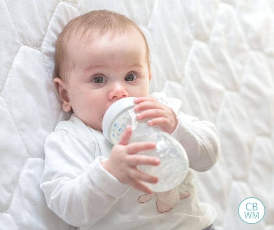 Baby drinking from bottle on a white blanket