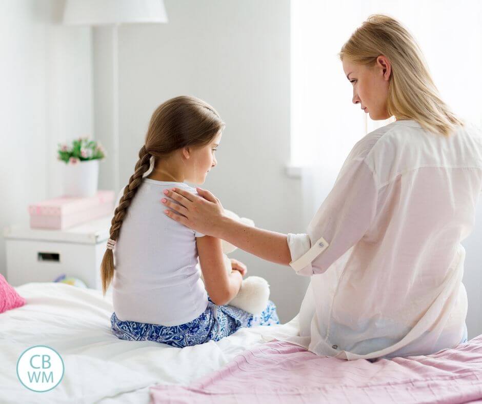 Mother consoling her sad daughter as they sit on a bed