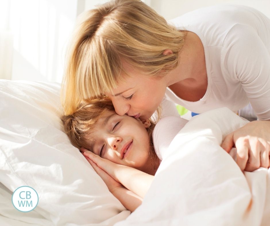 Child sleeping with sun in the room. Mom kissing cheek.