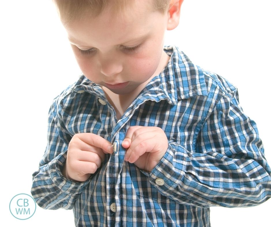 young boy buttoning up his shirt