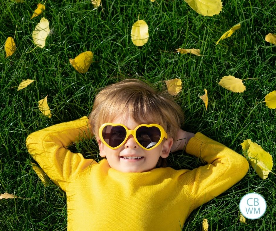 Child lying on the grass wearing a yellow sweater and yellow heart glasses