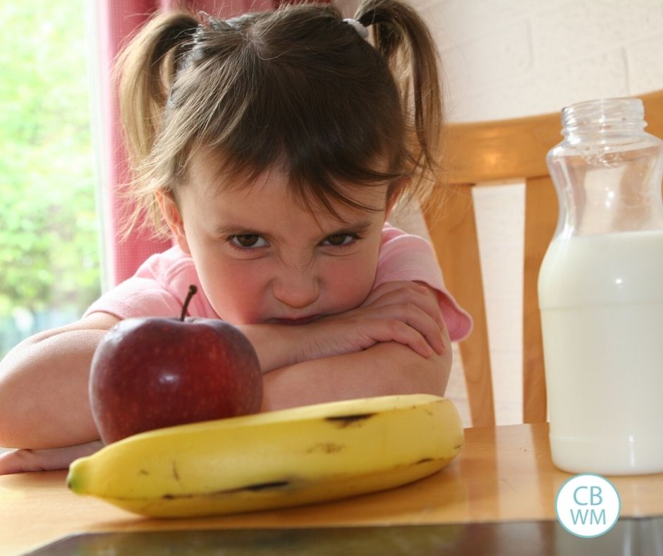 child looking with disgust at apple and banana