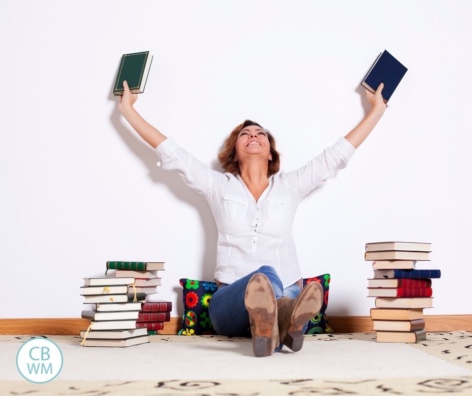 Mom holding a book up in each hand with piles of books beside her.