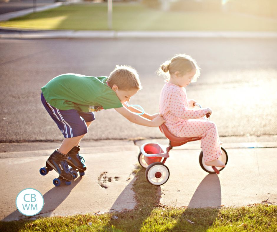 brother pushing his sister on a tricycle