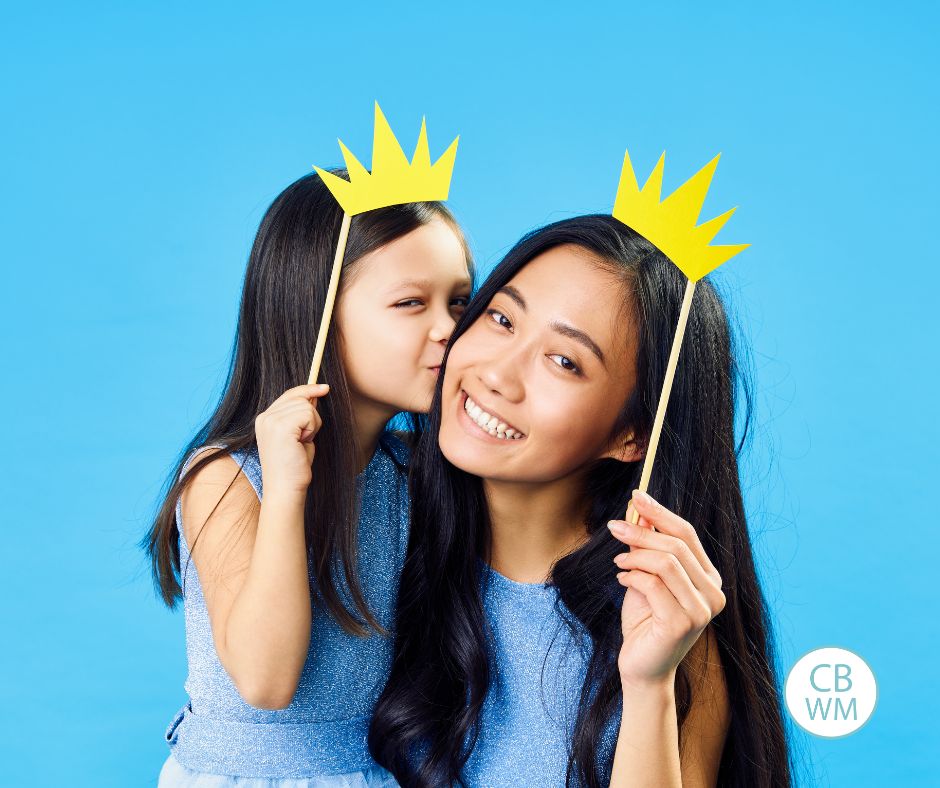 Mom and daughter holding paper crowns above their heads.