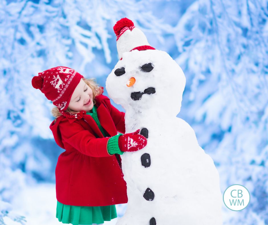 Girl building a snowman. She is putting the coal on the snowman