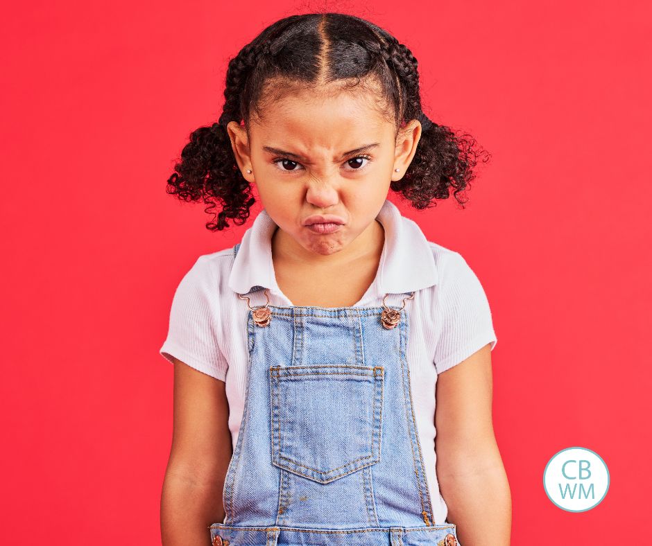 grumpy child scowling at the camera with a red background behind her