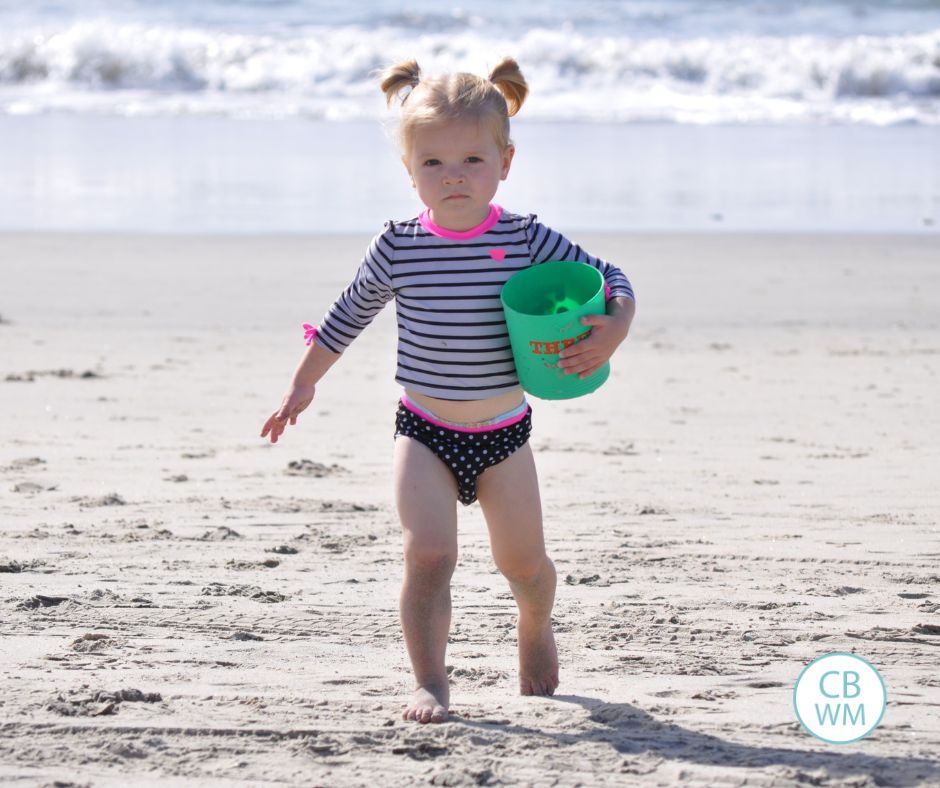 Brinley walking on teh beach while holding a bucket