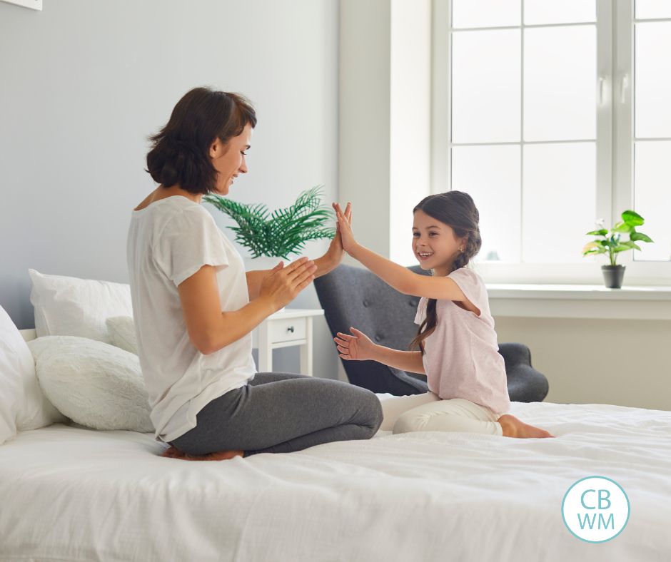 Mom and daughter clapping hands while sitting on a bed