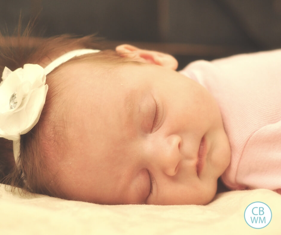 Baby girl sleeping on her tummy on a cream colored blanket