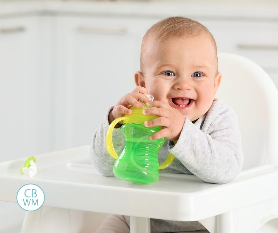 Smiling baby with a sippy cup smiling in a high chair