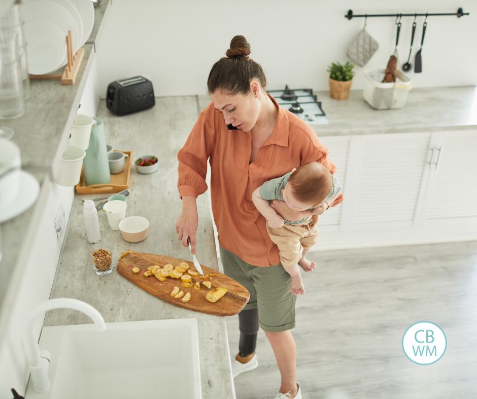 mom holding a baby while cutting up food