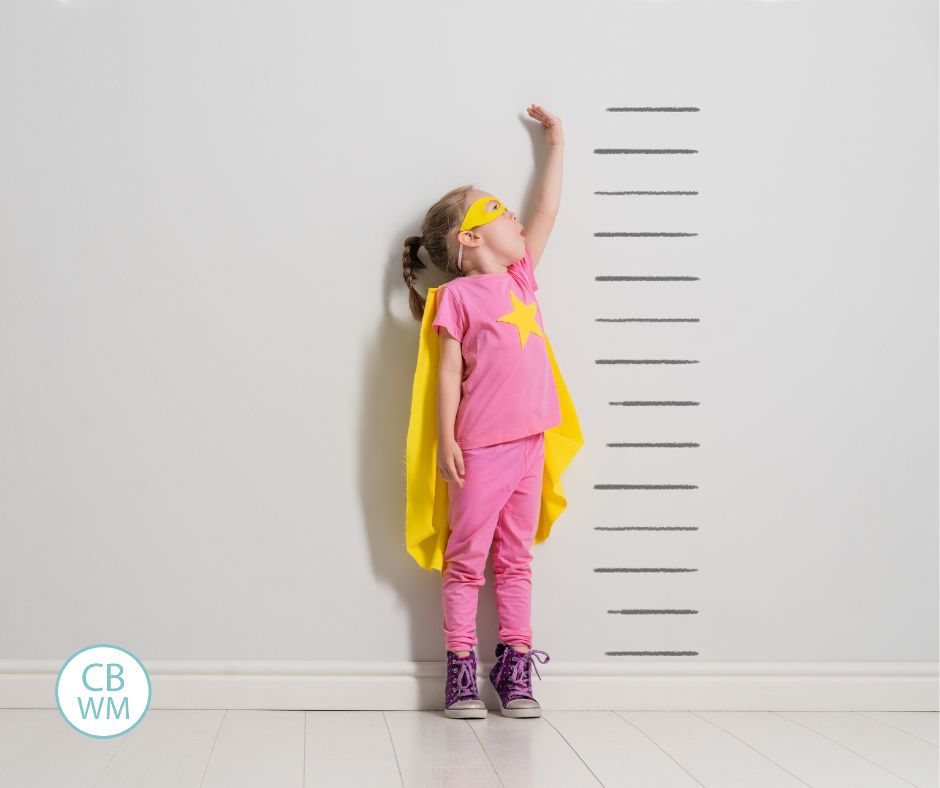 Child measuring herself while wearing suprehero cape