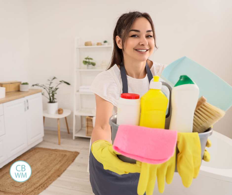 Woman clenaning a bathroom holding cleaning supplies