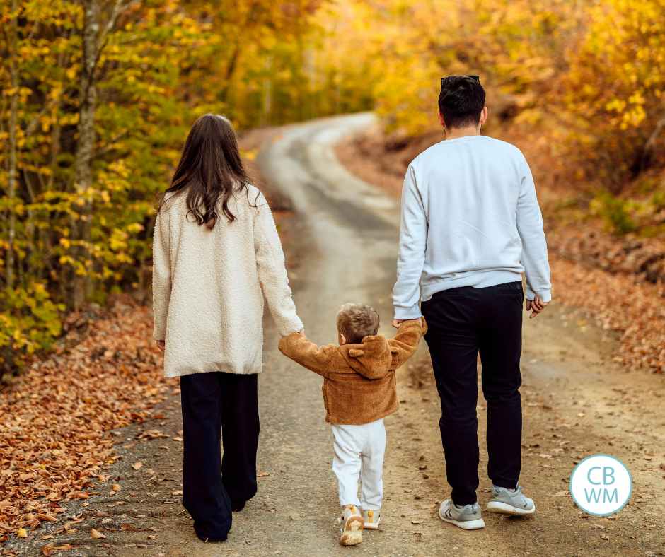 Mom, child, Dad walking along a path in the fall with beautiful autumn colors on the trees