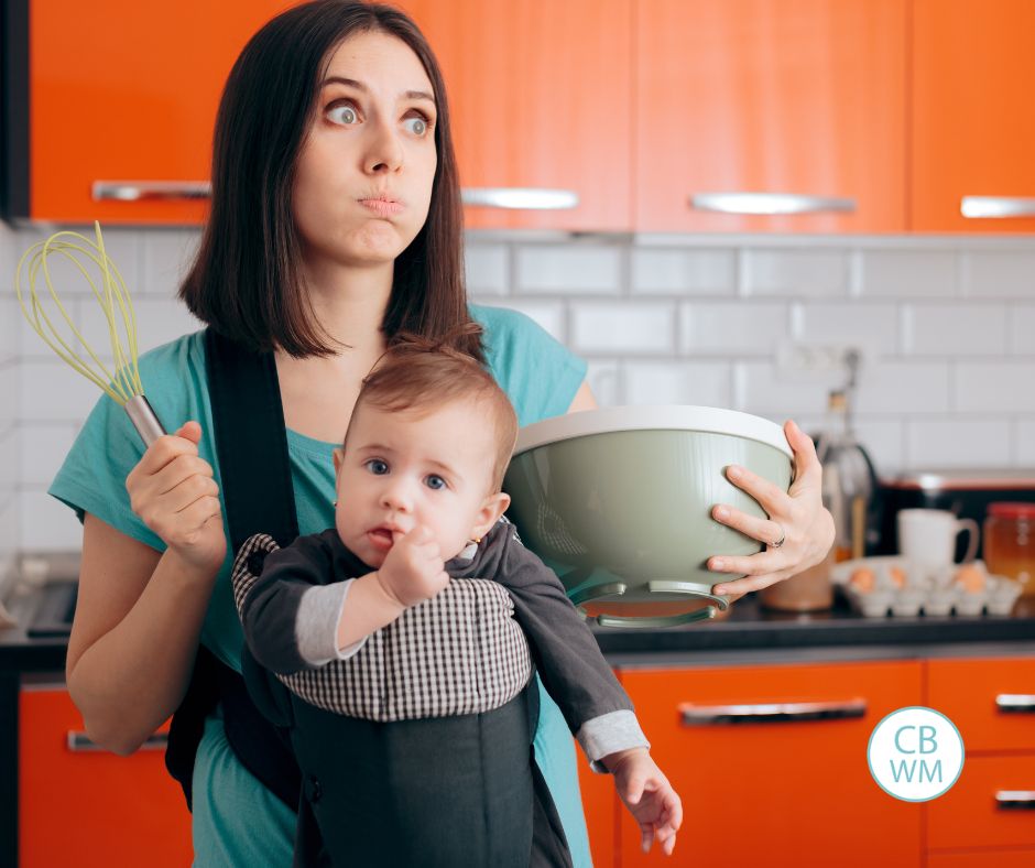 Mom holding a baby and a mixing bowl with an exasperated look on her face