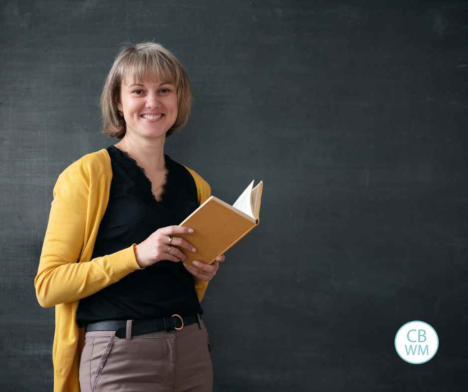 Teacher holding a book standing in front of a blackboard