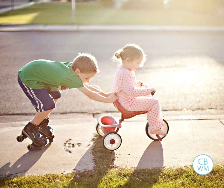 Boy wearing roller skates pushing his little sister on a tricycle