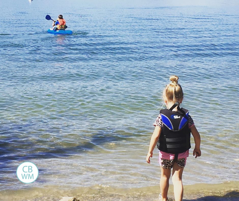 Brinley on the beach with Brayden in the water on a kayak