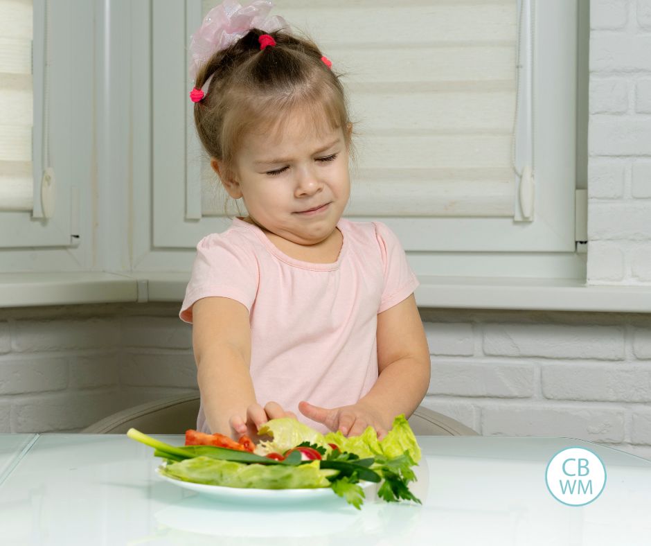 Girl wearing a pink shirt pushing away a plate of vegetables with a disgusted look on her face
