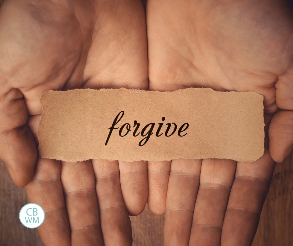 Hands holding a slip of paper that says "Forgive" on it