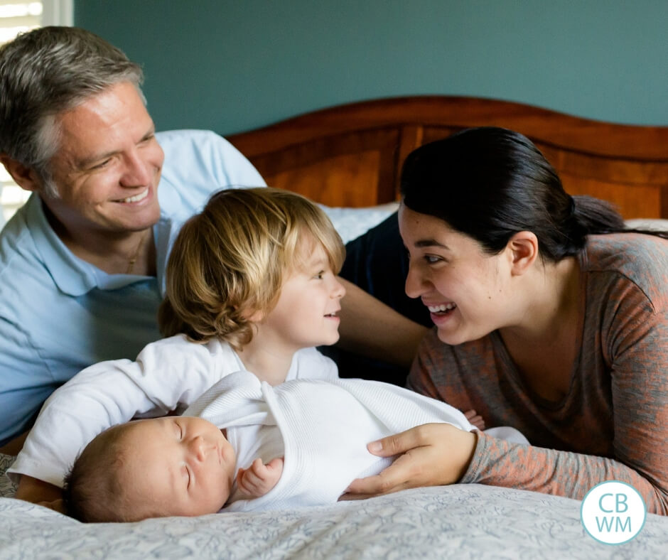 Family of four on a bed. New baby with older brother, mom, and dad