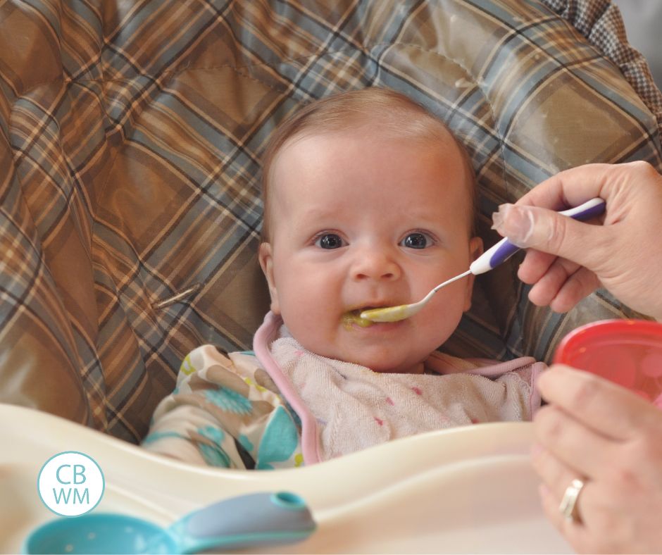 baby eating solid foods and looking at the camera