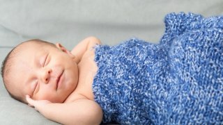 Baby sleeping on gray blanket with a blue blanket on top