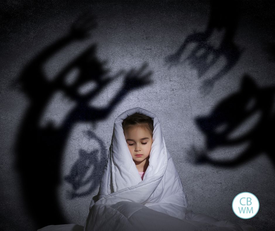 Child in bed with a blanket over her head and scary shadows on the wall