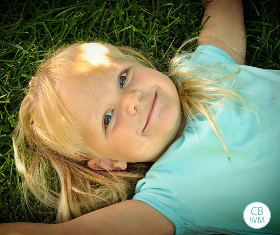 three year old girl with blonde hair lying on the grass