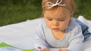 Baby on tummy on a blanket looking at a book