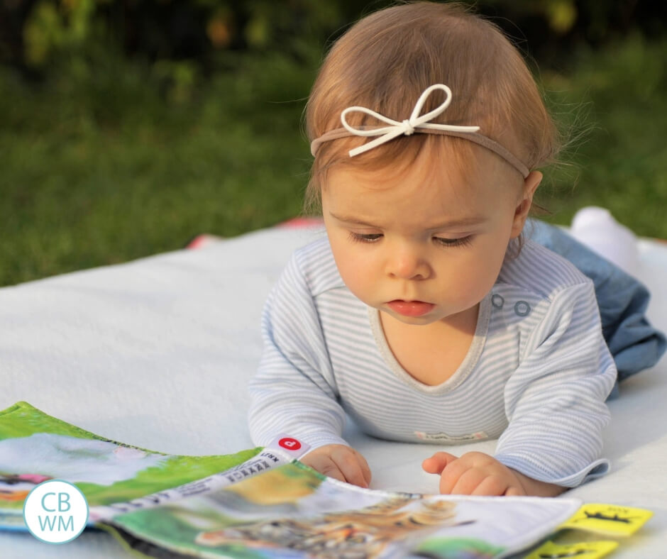 Baby on tummy on a blanket looking at a book