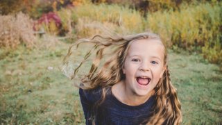 Girl running toward the camera with fall foliage behind her.