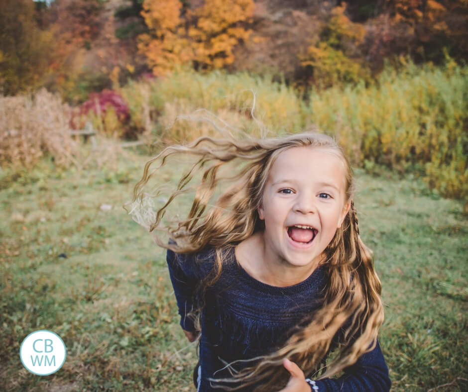 Girl running toward the camera with fall foliage behind her.