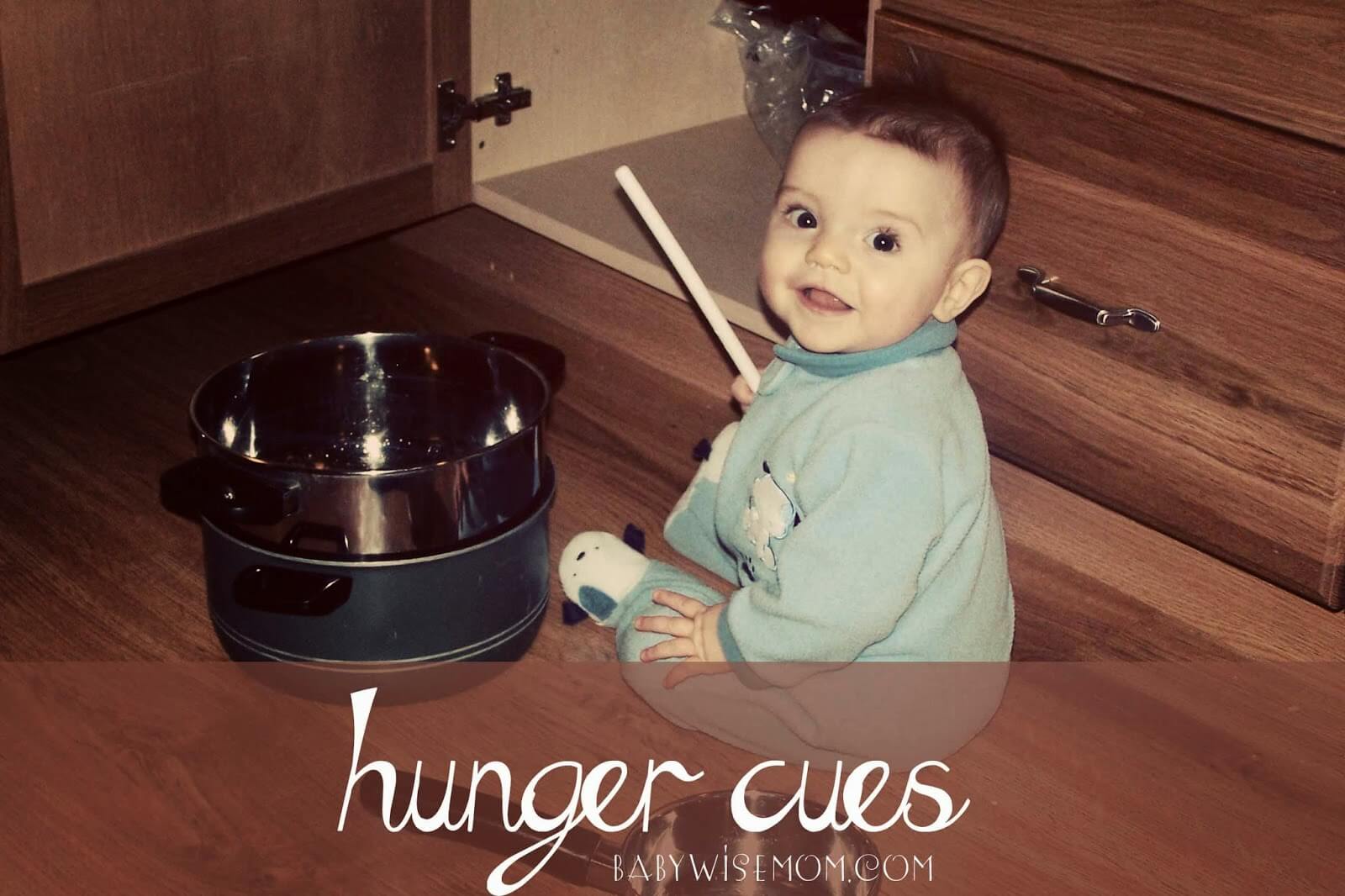 Baby boy sitting on the kitchen floor playing with pots and pans