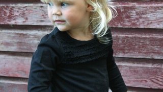 Toddler looking over her shoulder with a burgundy ship-lap background