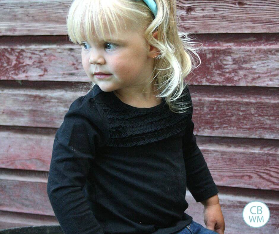 Toddler looking over her shoulder with a burgundy ship-lap background