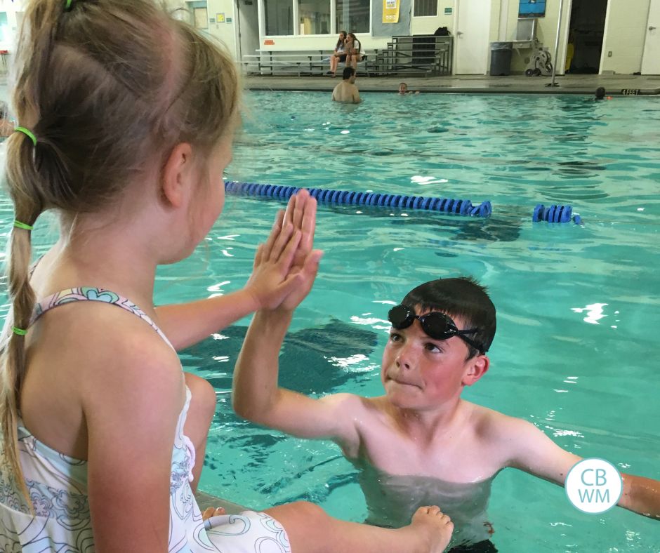 Brayden in the pool giving Brinley, sitting on the side, a high five