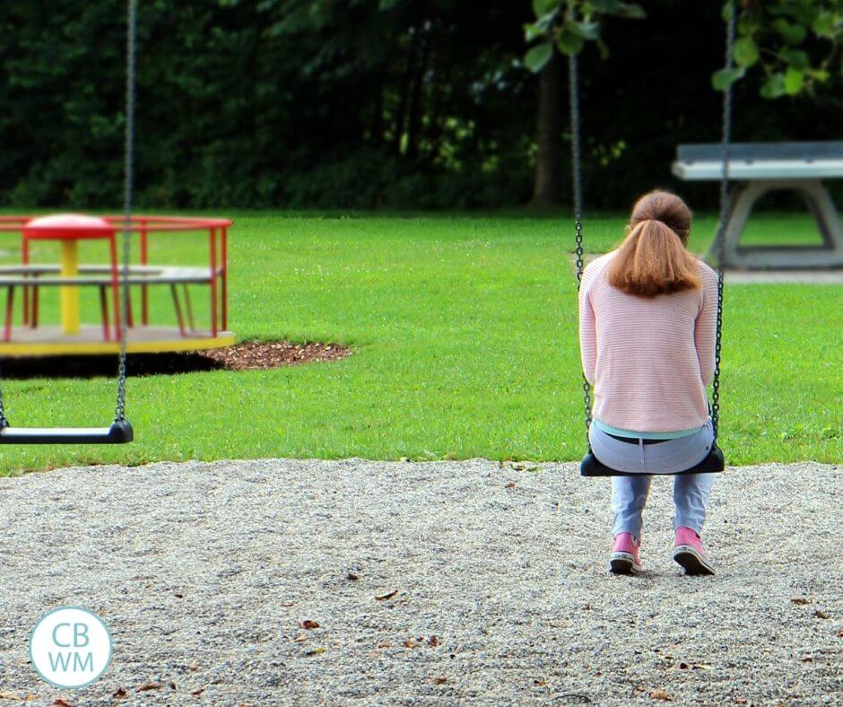 Woman sitting on swing with her head bowed in sadness