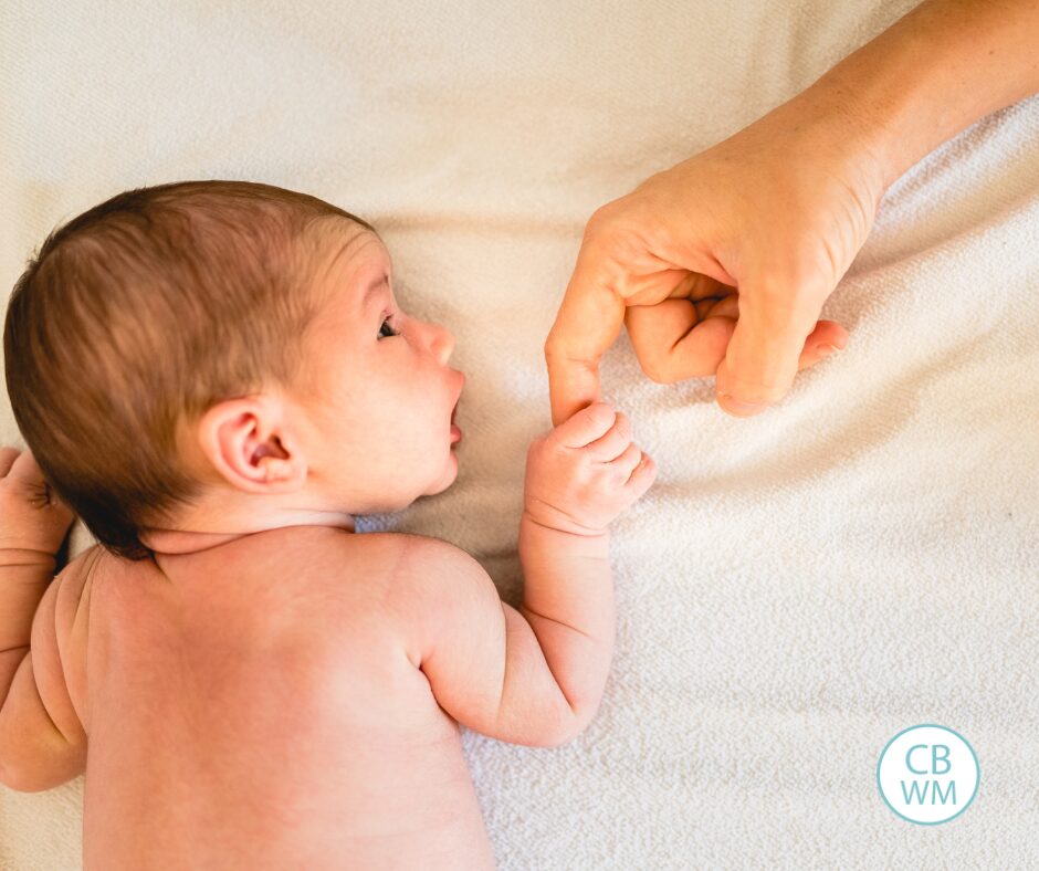 newborn laying on tummy and holding the finger of a parent